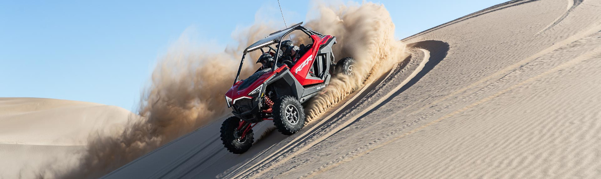 Two individuals in a Polaris® UTV, kicking up sand on a dune in the desert.